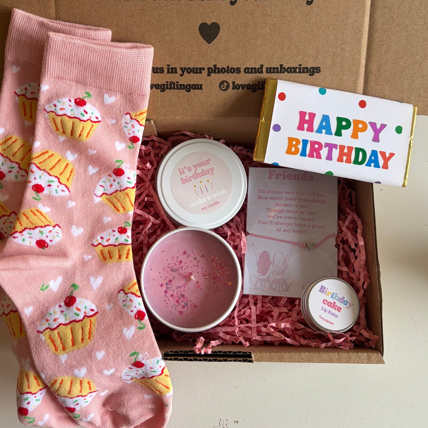 Birthday gift set with pink cupcake-patterned socks, a small bowl, and a 'Happy Birthday' card in a box.