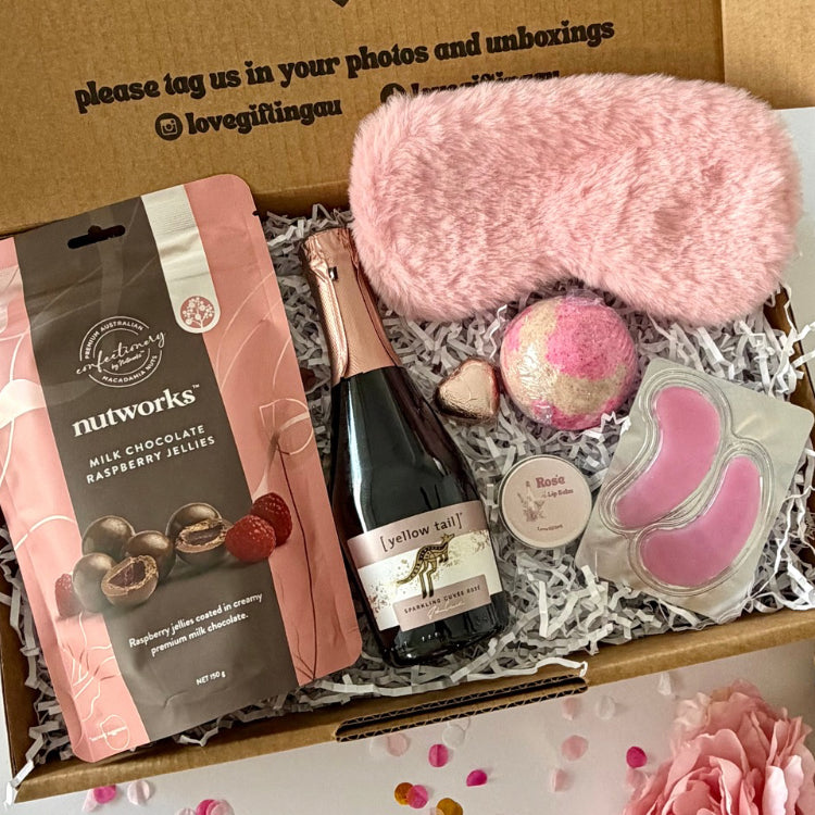 A curated self care birthday or pamper gift box  includes nutworks chocolate-covered raspberry jellies, a pink plush eye mask, a strawberry bath bomb, Rosé prosecco, Rosé lipbalm and pink under eye masks.