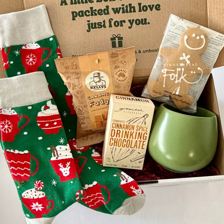 Christmas Cocoa & Cosy Toes gift box featuring festive hot chocolate socks, sage green ceramic mug, cinnamon drinking chocolate, caramel fudge and Gingerbread Folk gingerbread man.