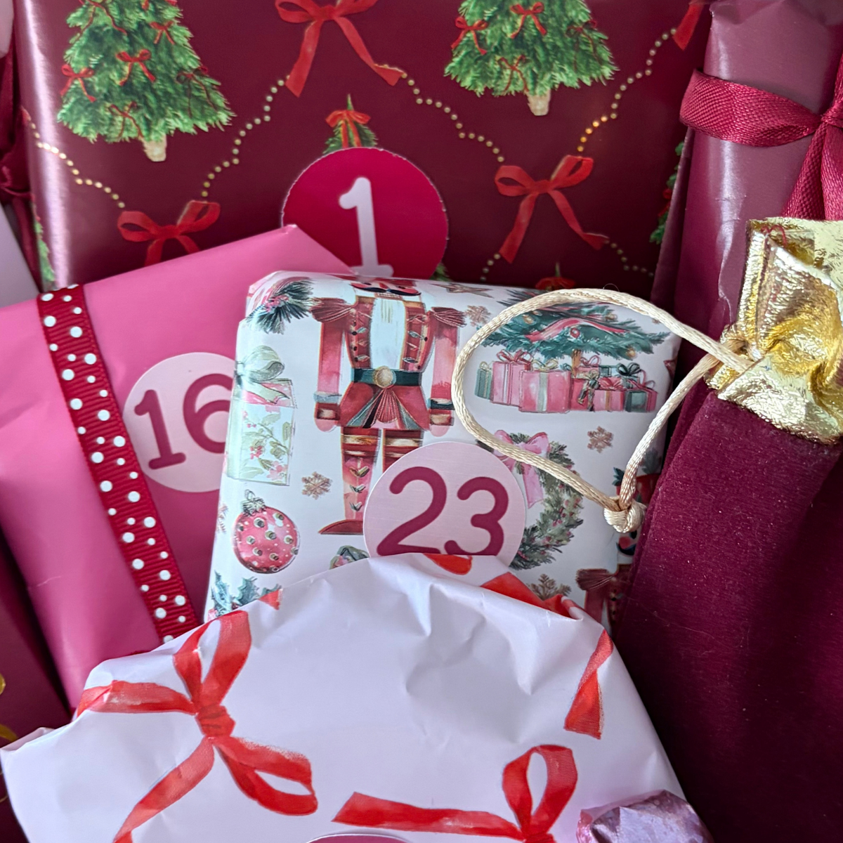 Close-up of numbered Christmas Advent gifts with festive nutcracker wrapping paper, pink ribbons and burgundy packaging inside Love Gifting's 24-Day Advent Box.