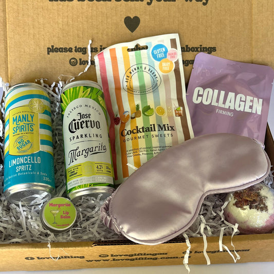 Gift box with items including a can, cocktail mix, and sleep mask on a white surface.