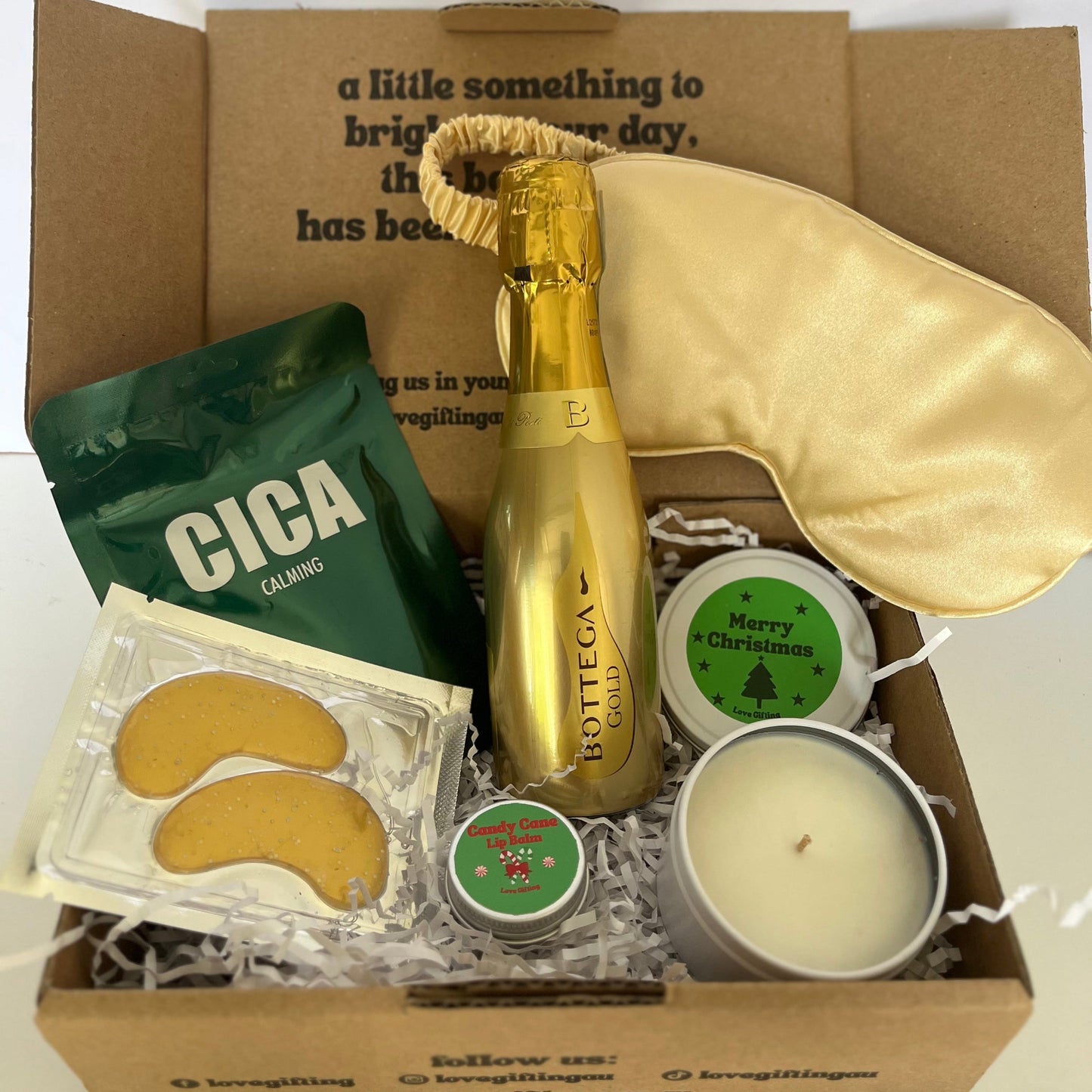 Gift box with a bottle of champagne, eye masks, and candles on a white background