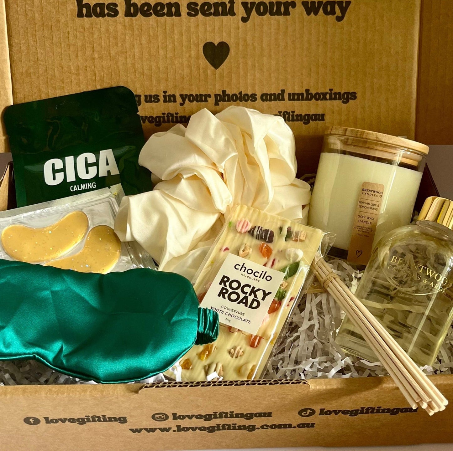 Gift box with various items including a candle, soap, and a bottle of oil, with a message on the box.