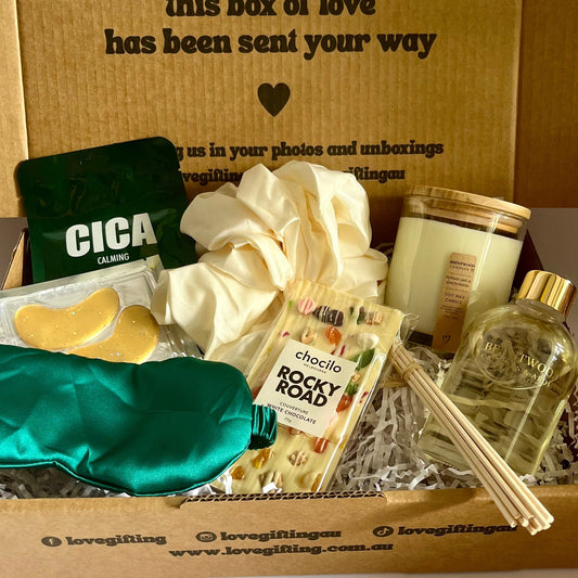 Gift box with various items including a candle, soap, and a bottle of oil, with a message on the box.