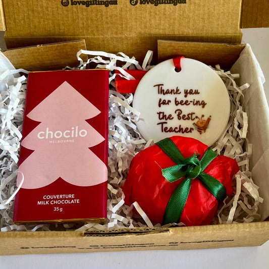 Gift box with a red chocolate bar, small plant, and wooden tag inside.