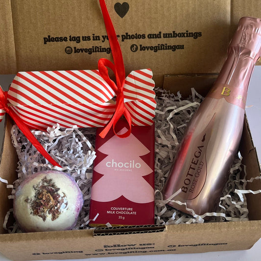 Gift box with a bottle of champagne, chocolate, and a decorative item on a white background.