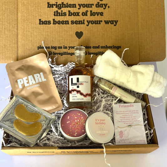 Gift box with various items including a bottle of gin, skincare products, and a candle, with a message on the lid.