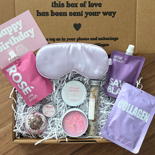 Gift box with self-care items including a sleep mask, bath bombs, and pouches on a wooden surface.
