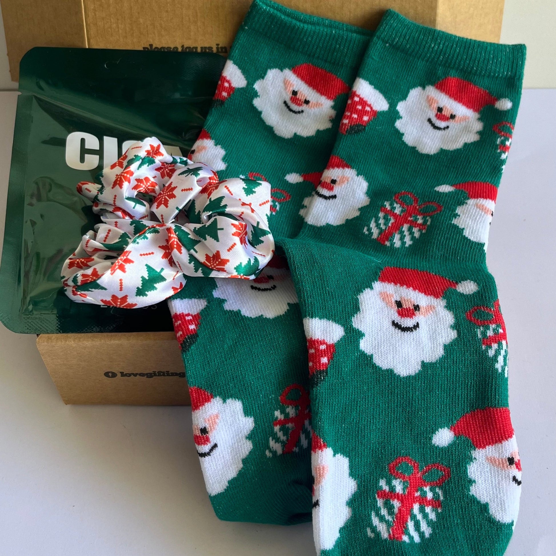 Green socks with Santa Claus design and a bow in front of a cardboard box.
