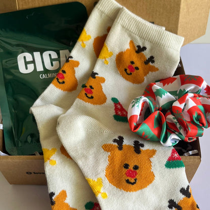 Pair of socks with reindeer design in a box with text and snacks.