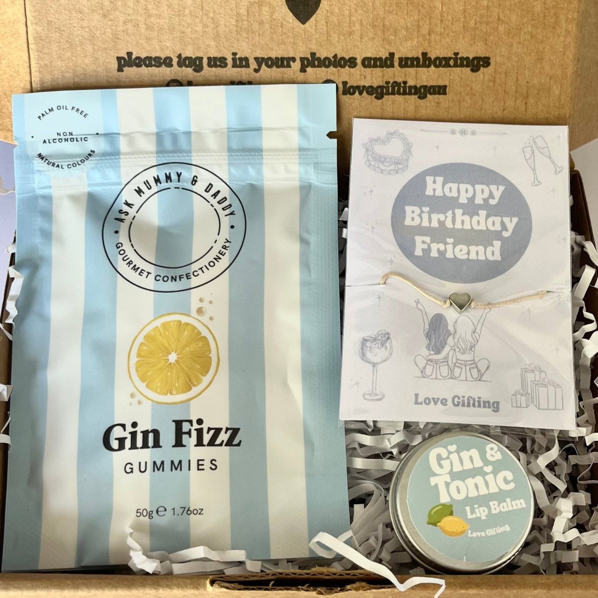 Gift box with 'Gin Fizz' gummies, a card, and a button with text on a white background.
