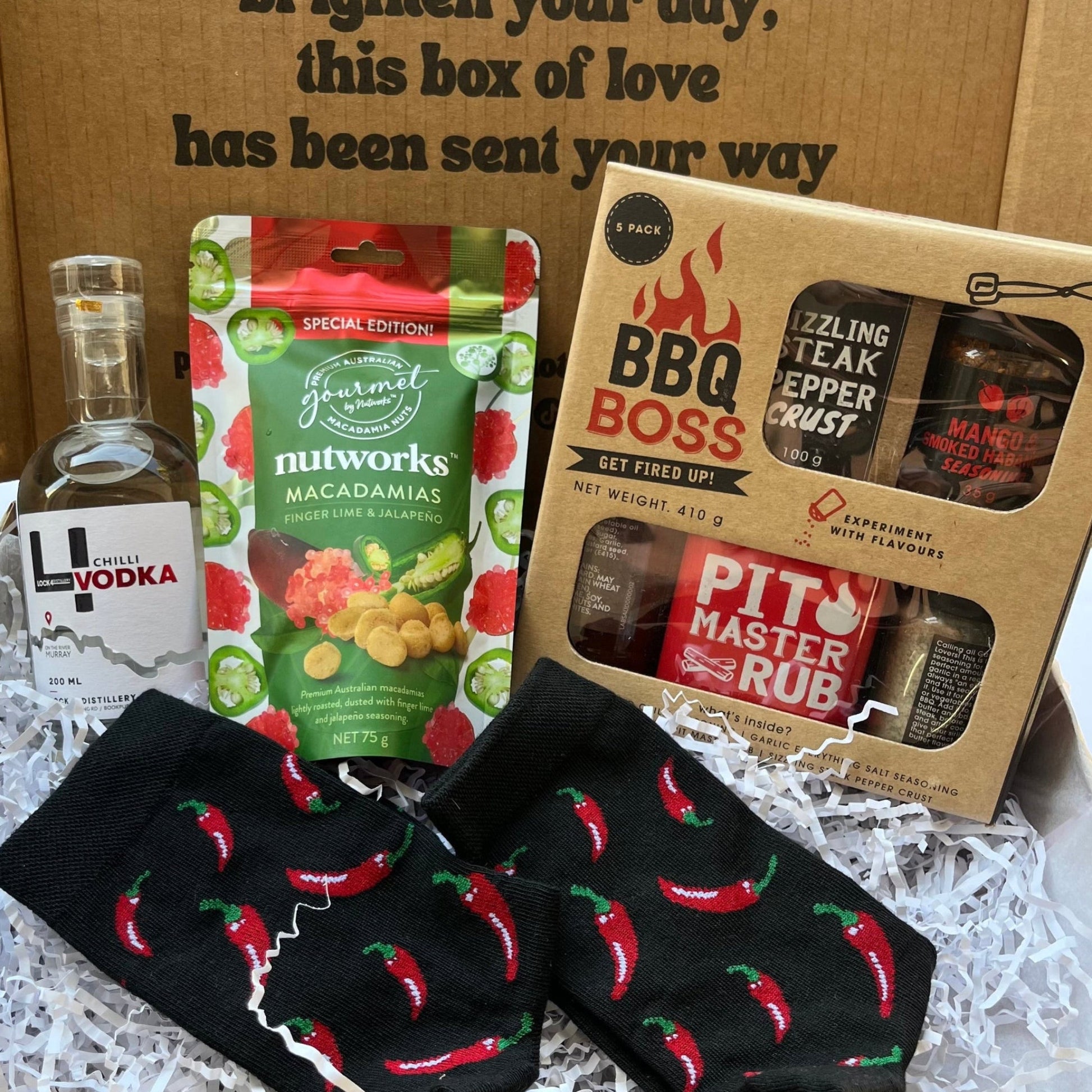 Gift box with BBQ-themed items including a bottle of vodka, macadamia nuts, and BBQ products.