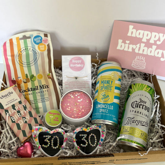 Gift box with birthday-themed items including drinks and a card on a white background