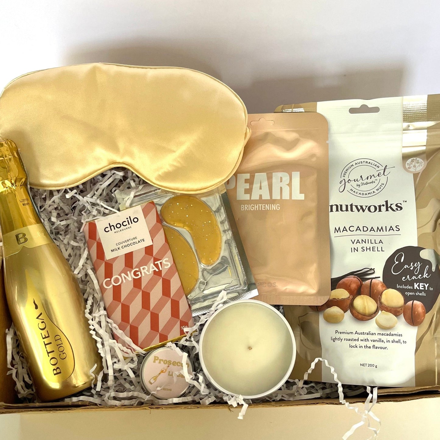 Gift box with champagne, sleep mask, and snacks on a white background