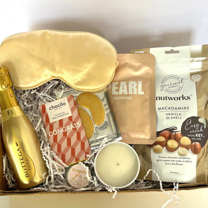 Gift box with champagne, sleep mask, and snacks on a white background