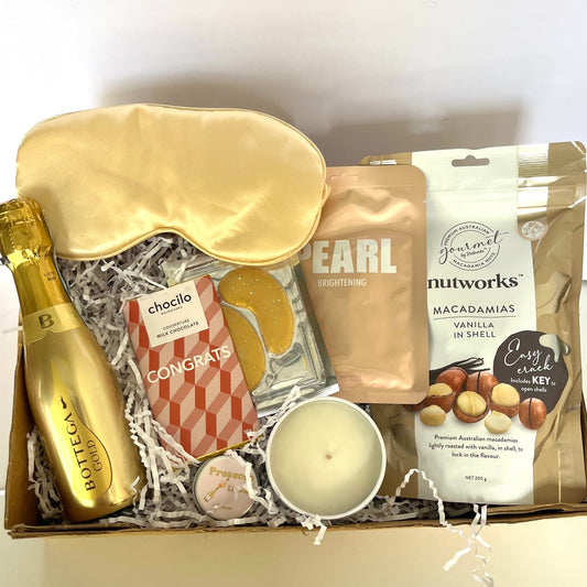 Gift box with champagne, sleep mask, and snacks on a white background