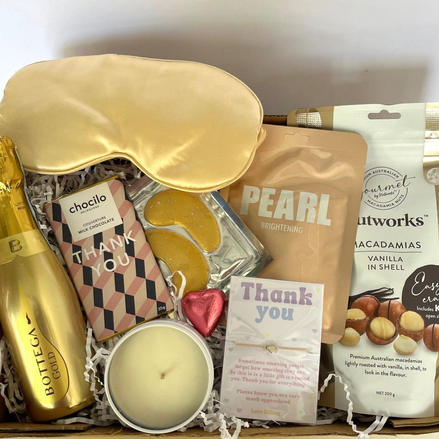 Gift box with champagne, sleep mask, and snacks on a white background