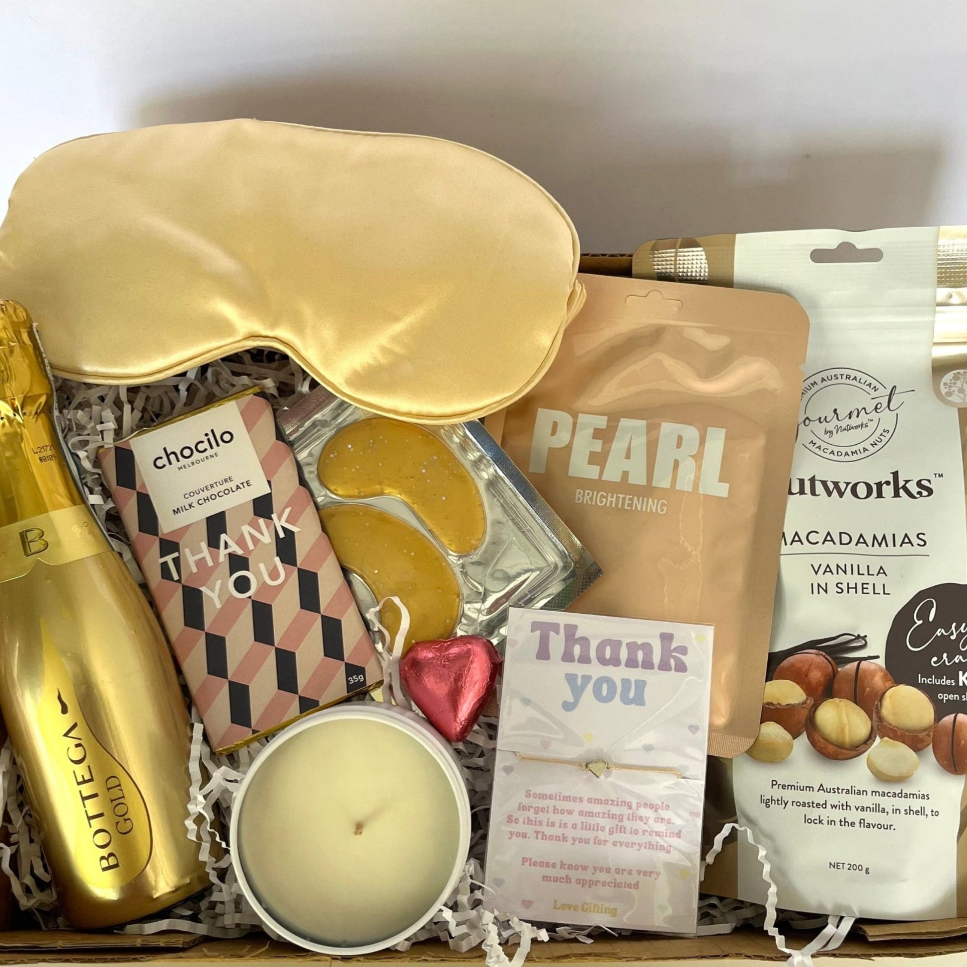 Gift box with champagne, sleep mask, and snacks on a white background