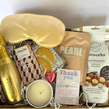 Gift box with champagne, sleep mask, and snacks on a white background