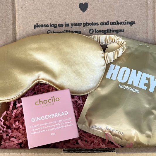 Box of self-care items including a sleep mask, gingerbread cookies, and a bag of honey with a message on the box.