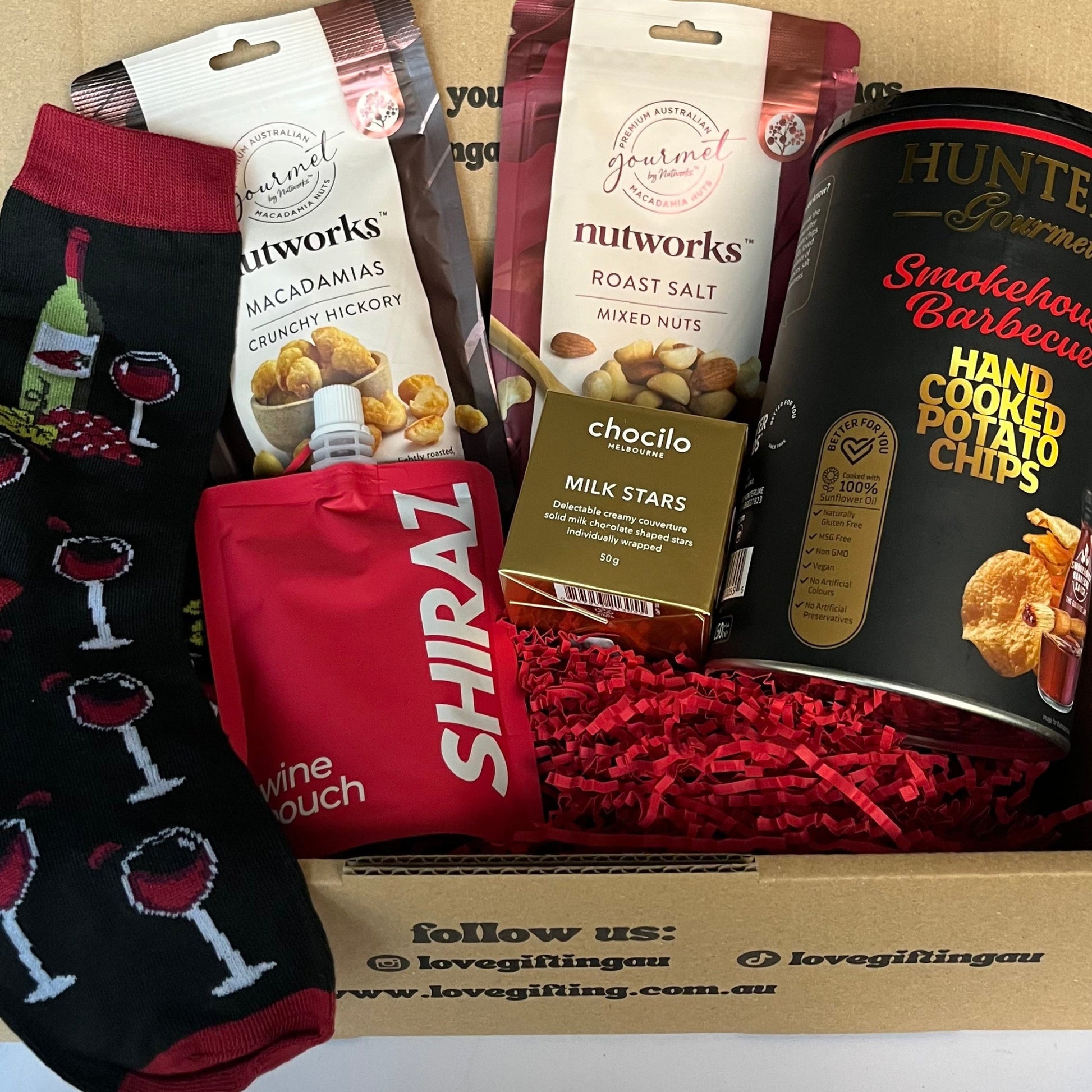 Gift box with snacks, wine-themed socks, and a card on a white surface
