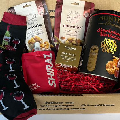 Gift box with snacks, wine-themed socks, and a card on a white surface