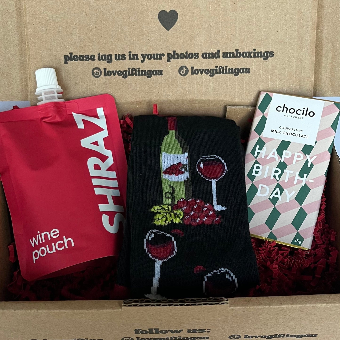 Box of love with wine-themed items including a pouch, socks, and a card.