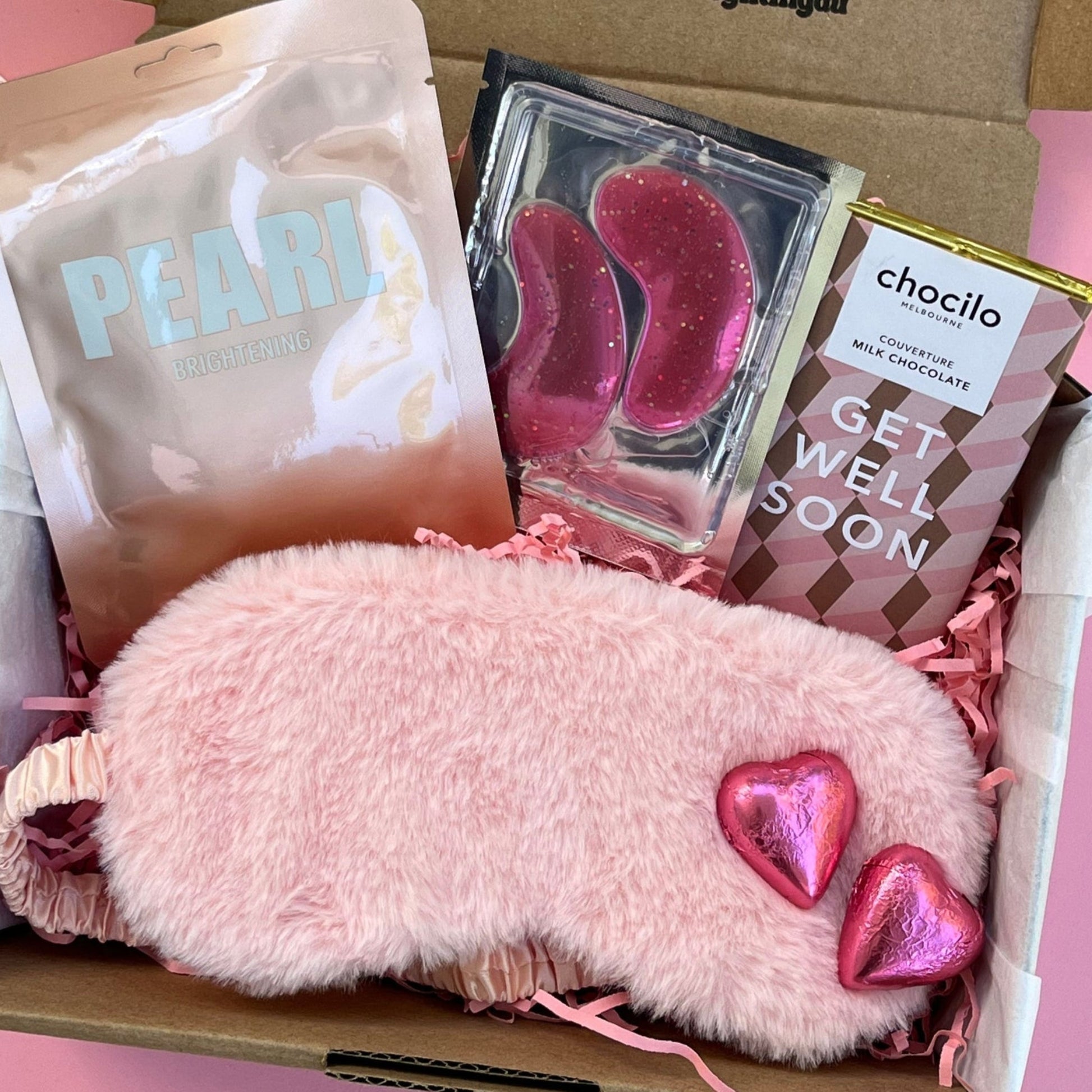 Gift box with pink fluffy eye mask, pink heart-shaped milk chocolates,  get well soon chocolate bar , Peral Lapcos sheet face mask, and under eye patches 