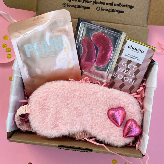 Gift box with pink fluffy eye mask, pink heart-shaped milk chocolates,  get well soon chocolate bar , Peral Lapcos sheet face mask, and under eye patches 