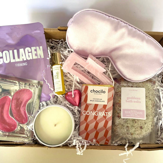 Gifting box with skincare products, a candle, and a sleep mask on a white background