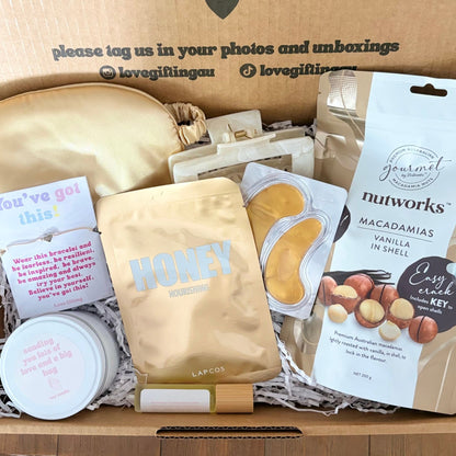 Gift box with various items including a jar, cookies, and a card, with text on the box.