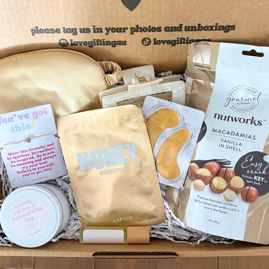 Gift box with various items including a jar, cookies, and a card, with text on the box.