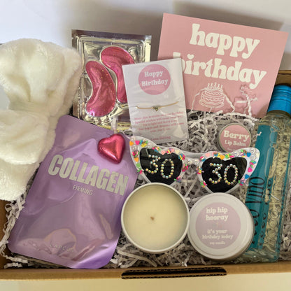 Gift box with various items including a candle, 'happy birthday' card, and 'collagen' package.