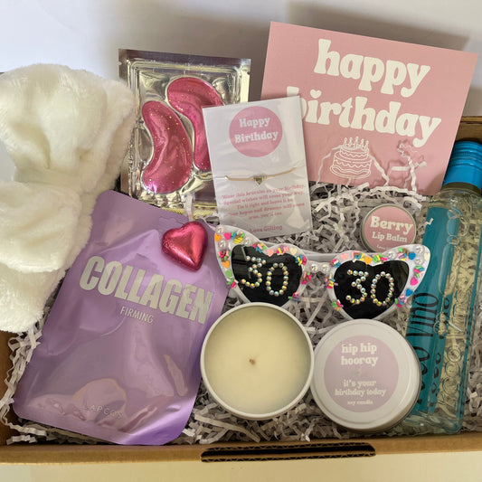 Gift box with various items including a candle, 'happy birthday' card, and 'collagen' package.