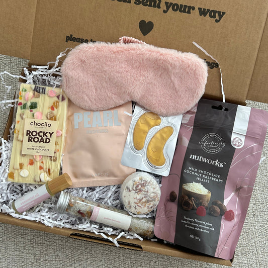 Unopened box with a pink eye mask, snack, and other items on a gray surface