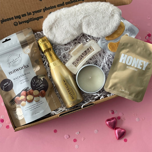 Gift box with champagne, snacks, and other items on a pink background