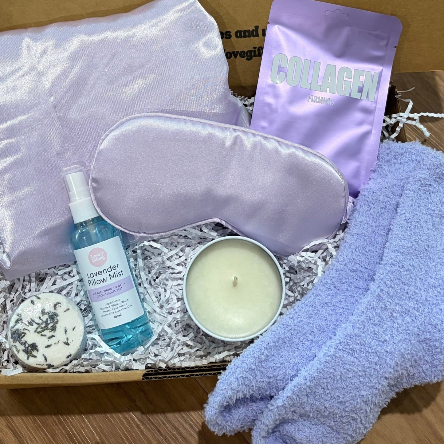 Gifting box with lavender shower steamer and pillow mist spray, purple socks. Satin pillowcase and eye mask and candle