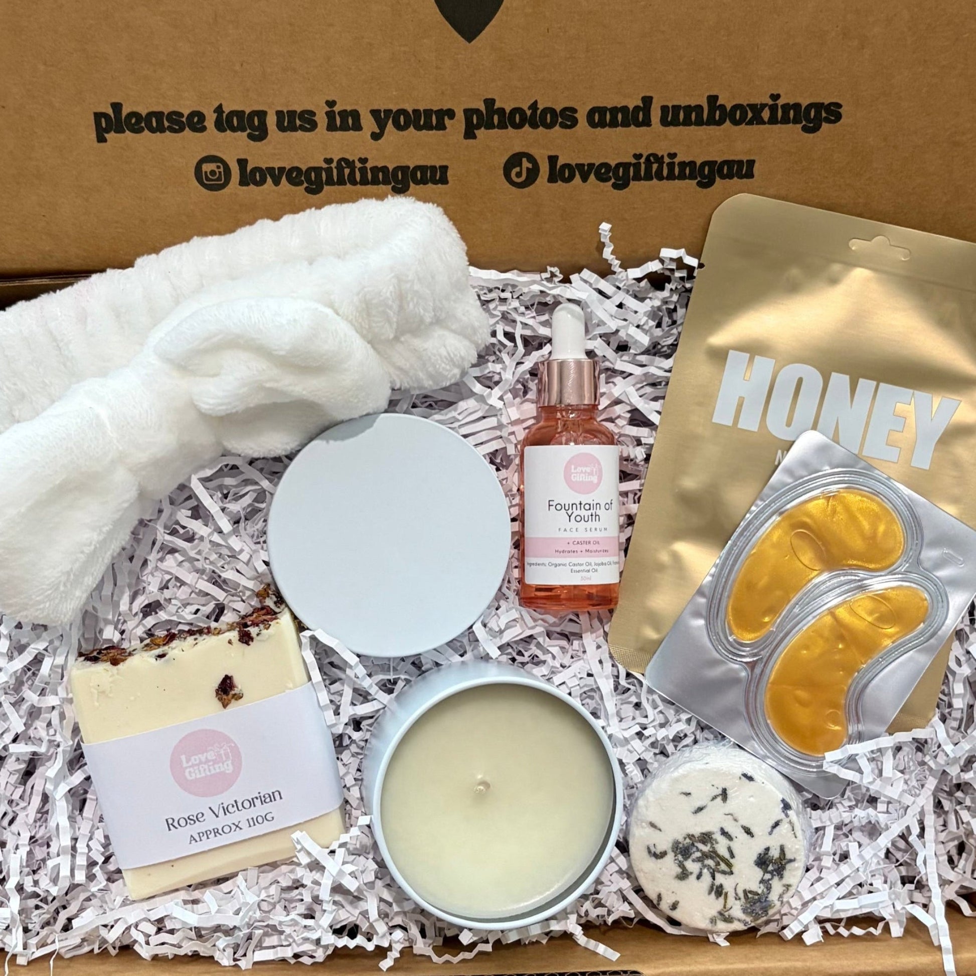 Self Care Pamper Gift box with various items including candles, a bottle, and wrapped products on a wooden surface.