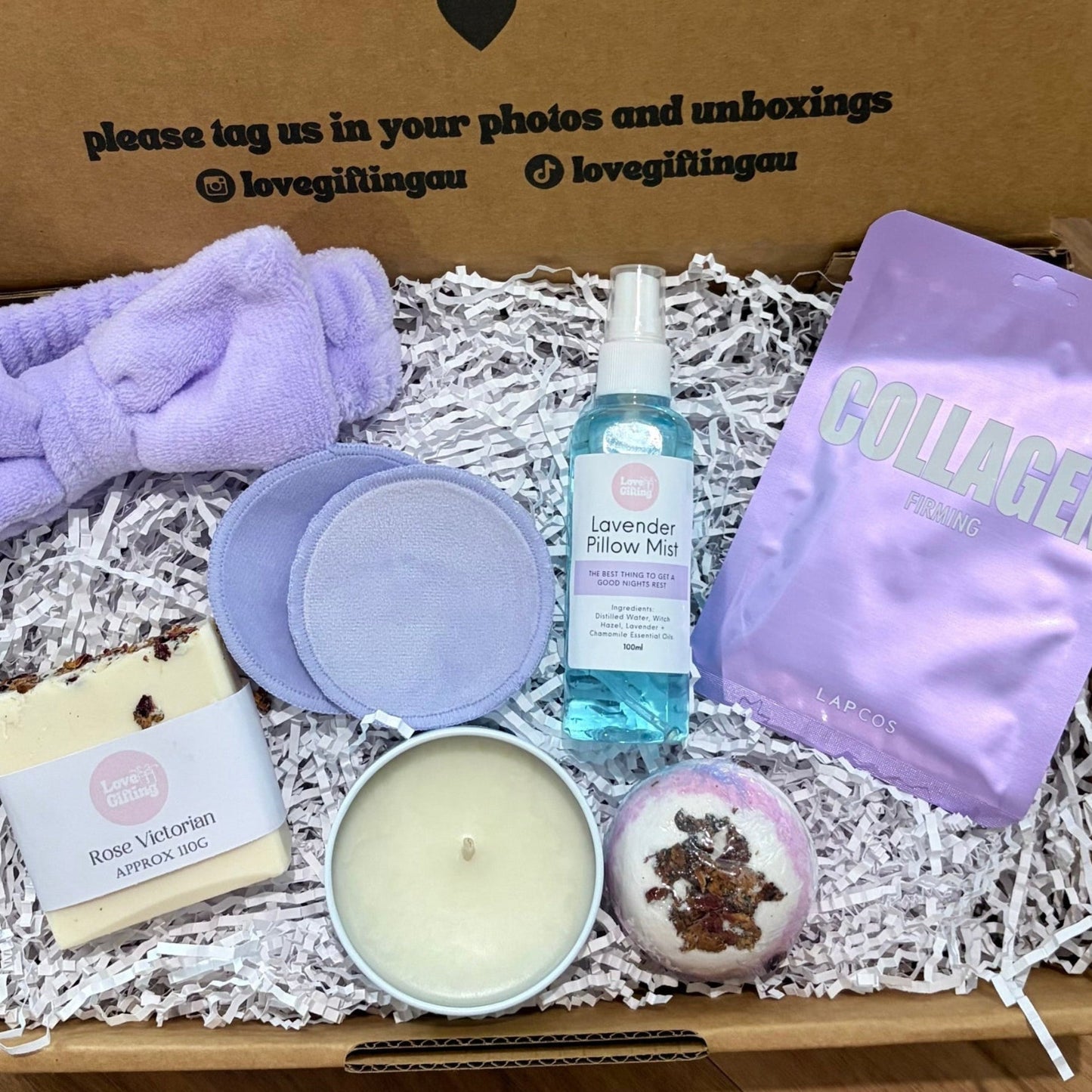 Gift box with various items including a candle, soap, and bath bombs on a wooden surface.