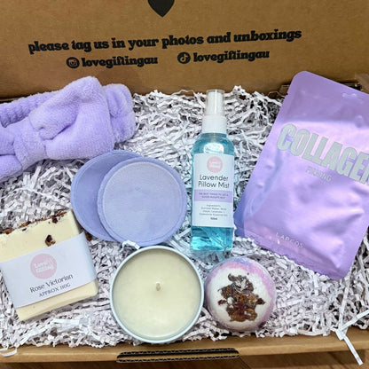 Gift box with various items including a candle, soap, and bath bombs on a wooden surface.