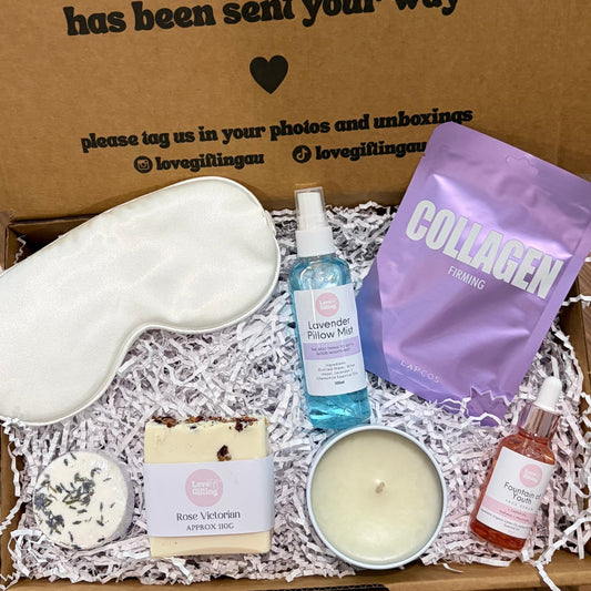 Gift box with self-care items including a sleep mask, candle, and bottle on a wooden surface.