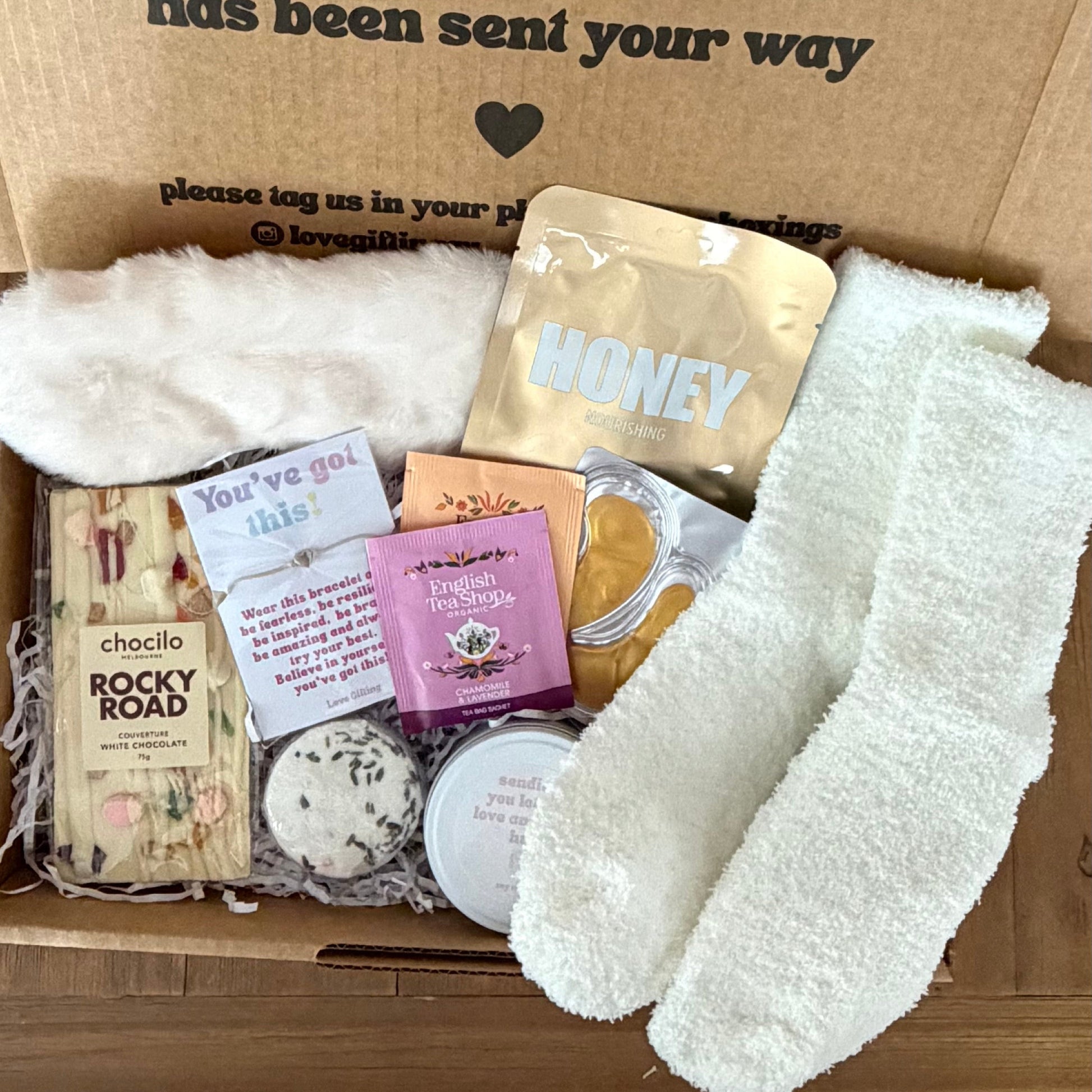 Box of care with socks, snacks, and a card on a wooden surface