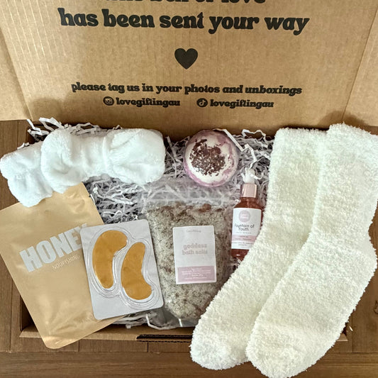 Unboxed gift box with white socks, skincare products, and a bow on a wooden surface.