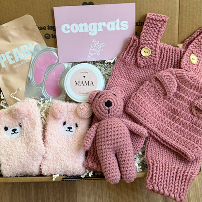 Gift box with pink baby items and a 'congrats' card on a wooden surface