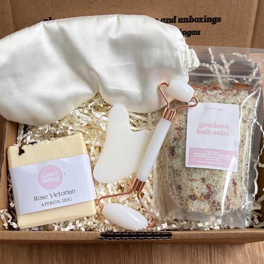 Gift box with bath items including a candle, soap, and bath salts on a wooden surface.