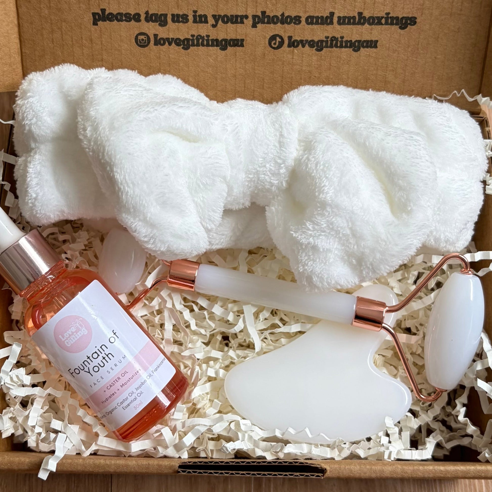 Gift box with a bottle, towel, and seashell on a wooden surface