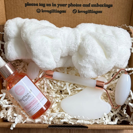 Gift box with a bottle, towel, and seashell on a wooden surface