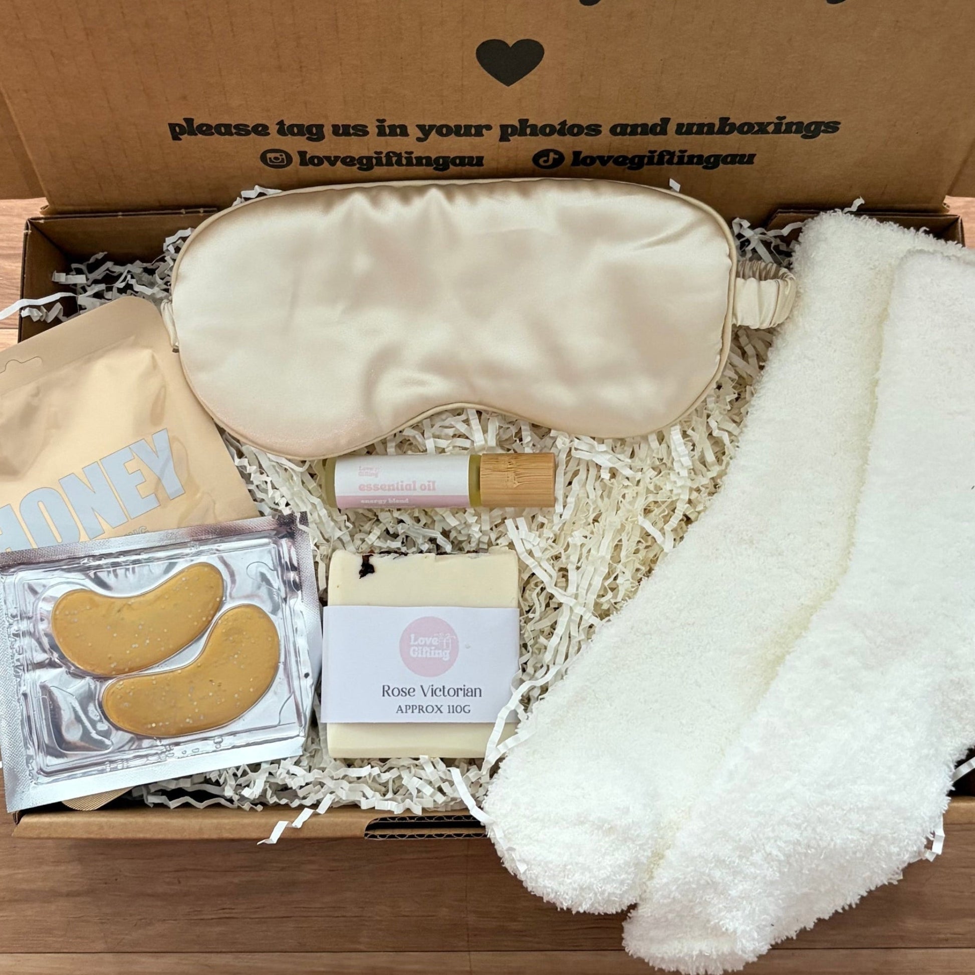 Gift box with sleep mask, socks, and other items on a wooden surface