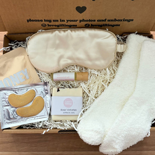 Gift box with sleep mask, socks, and other items on a wooden surface