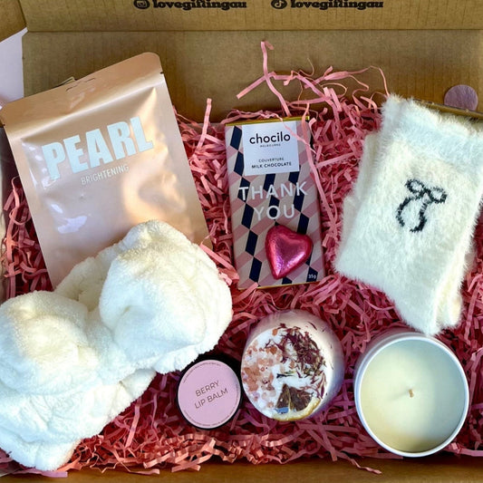 Gift box with various items including a candle, bath bomb, and 'thank you' card on a white background.